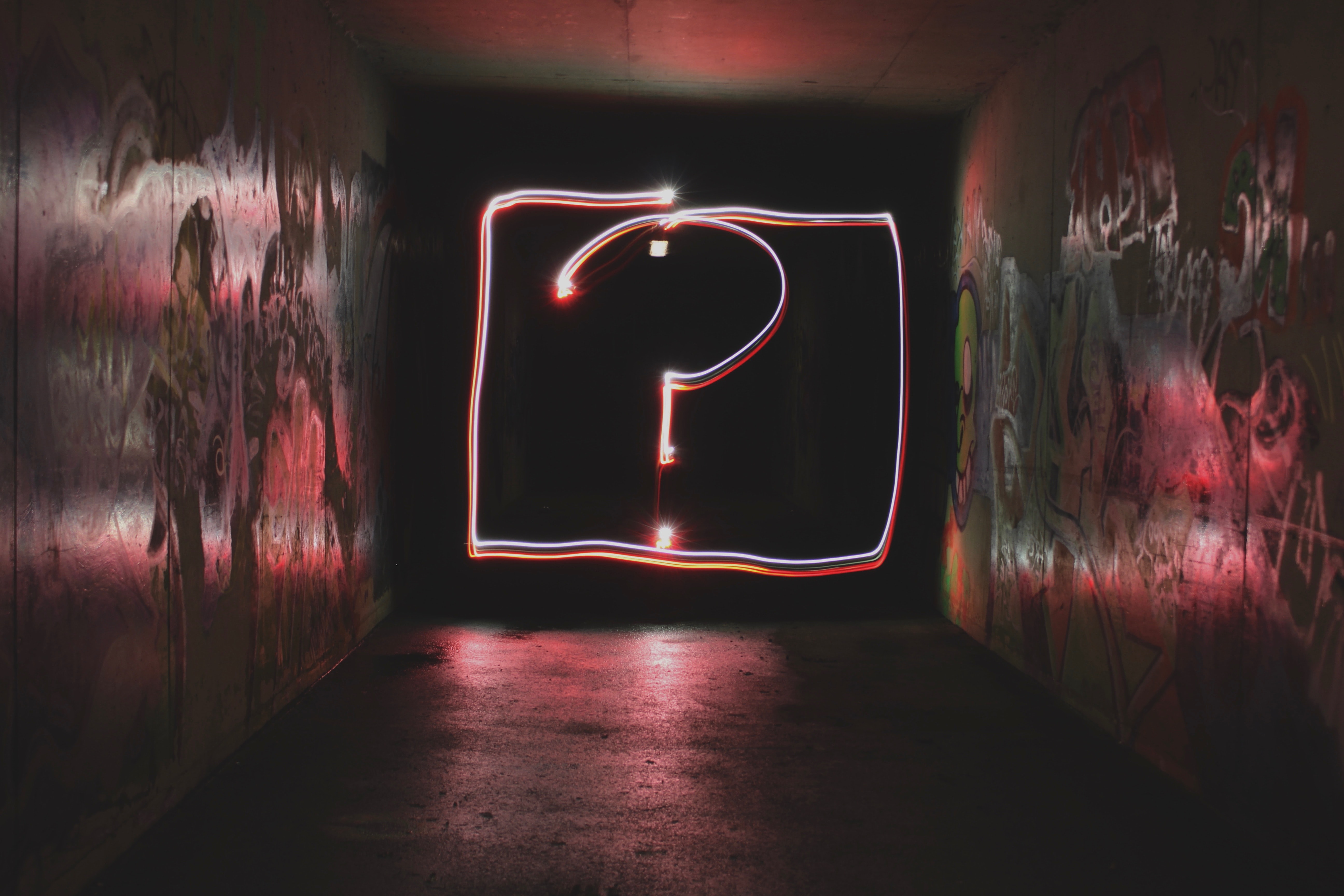 Red and white questions mark drawn with light photography in a dark laneway